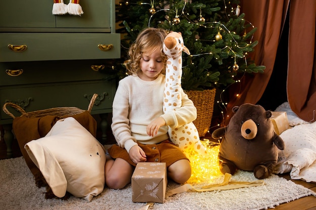 Petite fille dans la maison de Noël près d'une guirlande festive et étreignant ses jouets mignons