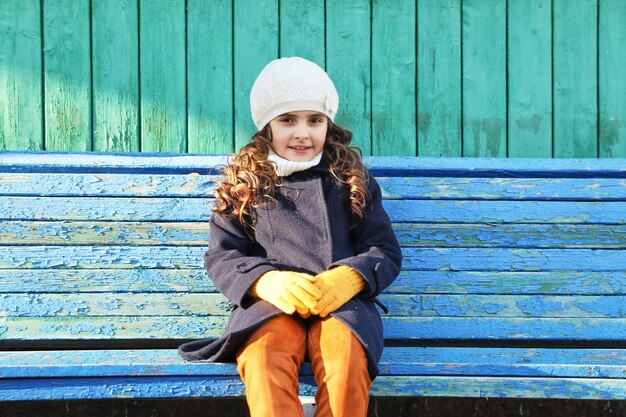 Petite fille dans un manteau bleu sur un banc de parc en automne. photo de haute qualité