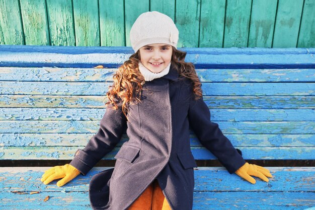 Petite fille dans un manteau bleu sur un banc de parc en automne. photo de haute qualité