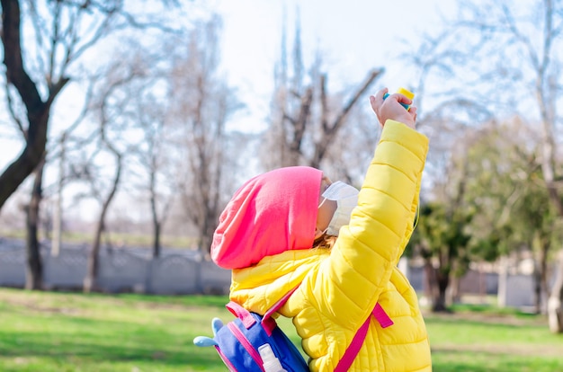 Une petite fille dans un masque de protection pendant la quarantaine se promène à l'extérieur au printemps et prend des photos avec un appareil photo pour enfants. Coronovirus, Covid-19.