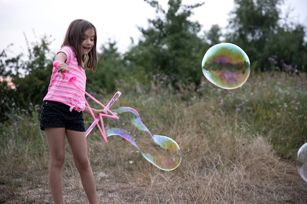 Une petite fille dans la nature joue avec de grosses bulles de savon.