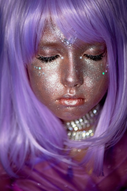 Une petite fille dans une perruque violette avec des paillettes argentées sur son visage Un monde imaginaire extraterrestreUne fée ou un extraterrestre Les yeux fermés Un visage paisible et calme