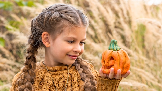 Petite fille dans un pull se penche sur une citrouille artificielle pour Halloween.