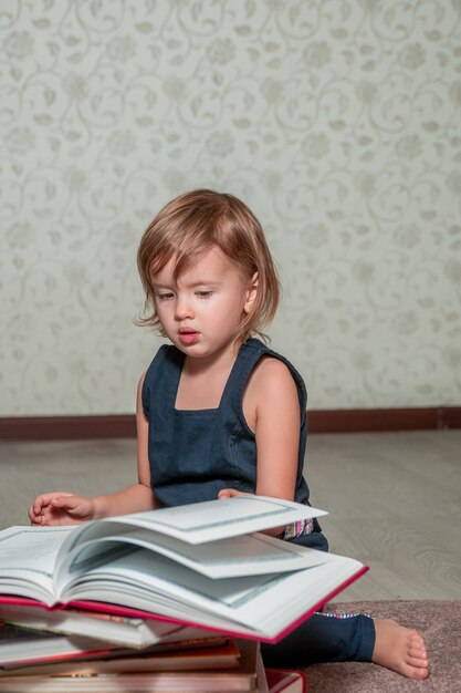 Une petite fille dans une robe bleu foncé lisant un livre assis sur le sol près de l'ours en peluche. L'enfant lit l'histoire pour le jouet. Tourne la page.