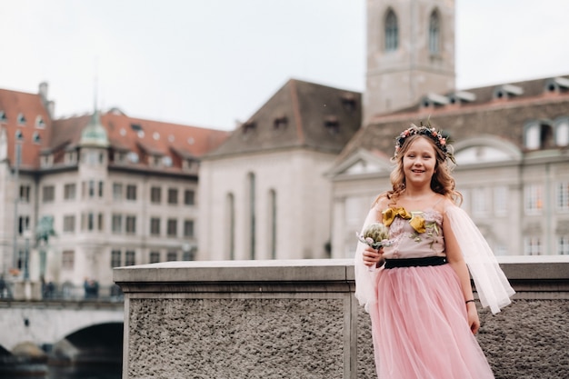 Une petite fille dans une robe princesse rose avec un bouquet dans ses mains se promène dans la vieille ville de Zurich.