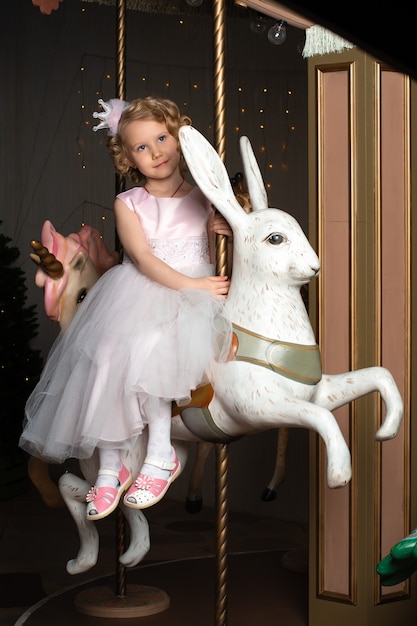 Une petite fille dans une robe rose et une couronne sur un carrousel avec un lièvre blanc.