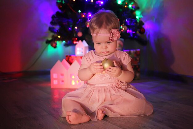 Une petite fille dans une robe rose, sur fond de sapin de Noël