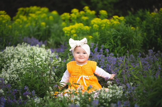 Petite fille dans une robe tricotée jaune se trouve parmi les fleurs dans le parc au printemps.