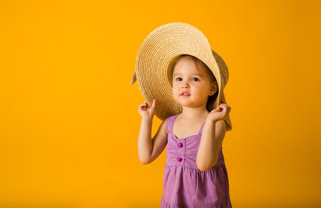 Petite fille dans une robe violette et un chapeau de paille sur une surface jaune avec un espace pour le texte