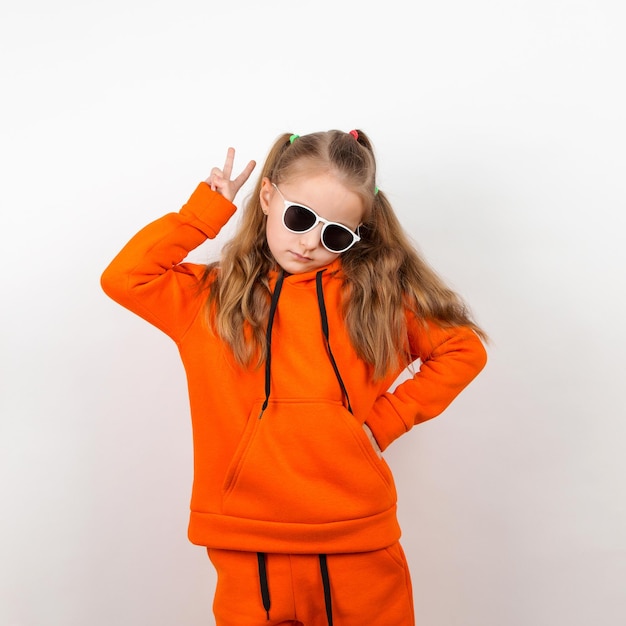 Une petite fille dans un sweat à capuche orange et des lunettes de soleil émotions de joie et un portrait de journée ensoleillée sur fond blanc