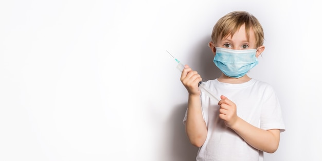 Petite fille dans un t-shirt blanc et un masque médical jouant au docteur tenant une seringue