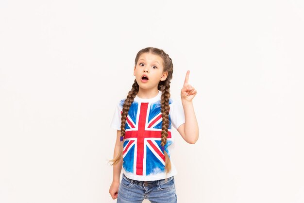 Une petite fille dans un T-shirt avec le drapeau de la Grande-Bretagne pointe vers votre publicité sur un fond blanc isolé