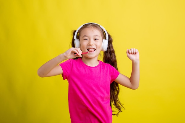 Une petite fille dans un T-shirt rose avec des écouteurs chante sur un fond jaune