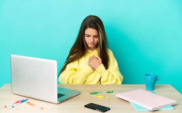 Petite fille dans une table avec un ordinateur portable sur fond bleu isolé ayant une douleur au cœur