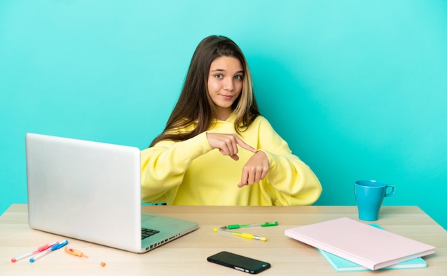 Petite fille dans une table avec un ordinateur portable sur fond bleu isolé faisant le geste d'être en retard
