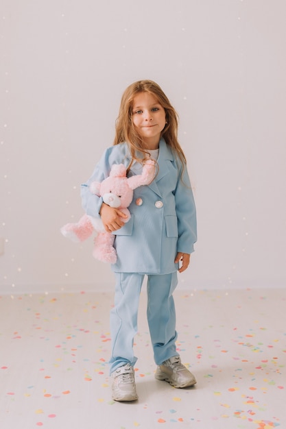 Petite fille dans un tailleur-pantalon bleu d'affaires avec un lapin jouet dans ses mains se dresse sur un fond gris