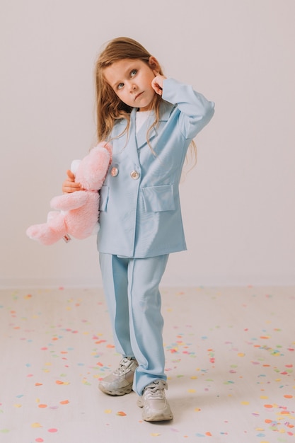 Petite fille dans un tailleur-pantalon bleu d'affaires avec un lapin jouet dans ses mains se dresse sur un fond gris