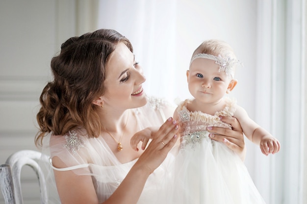 Petite fille dans une tendre étreinte de mère à la fenêtre. Mère tenant un petit enfant dans la fenêtre. Belle jeune maman et sa fille.