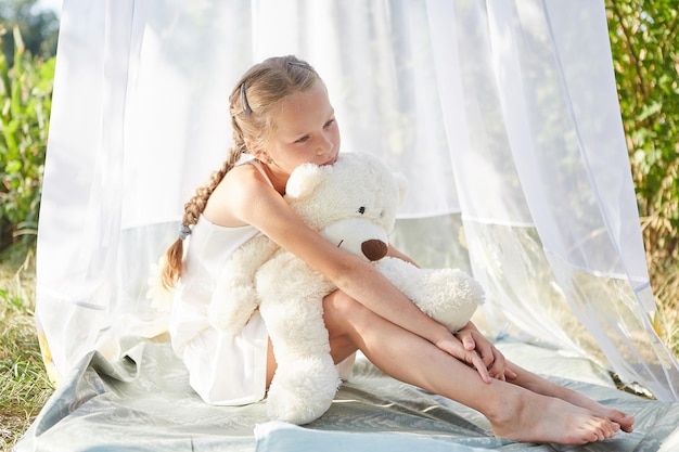 Petite fille dans une tente en mousseline blanche avec jouet