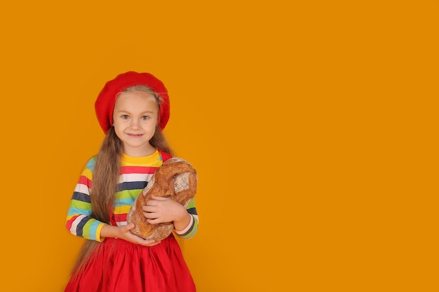 une petite fille dans une tête de béret rouge dans un Tshirt coloré dans une jupe rouge tenant du pain dans ses mains