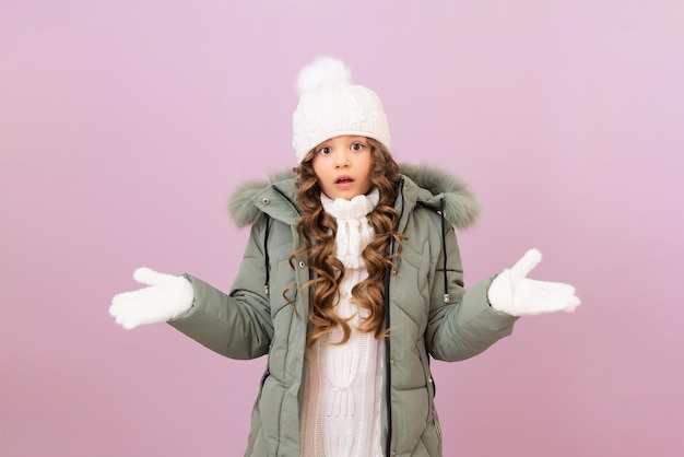 Une petite fille dans une veste d'hiver chaude et un bonnet tricoté et des cheveux bouclés sur un fond isolé. des vêtements chauds pour un hiver froid.