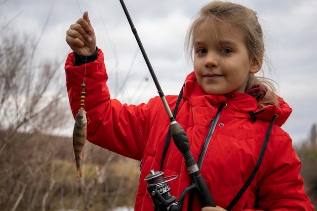 Petite fille dans une veste rouge avec un poisson dans ses mains