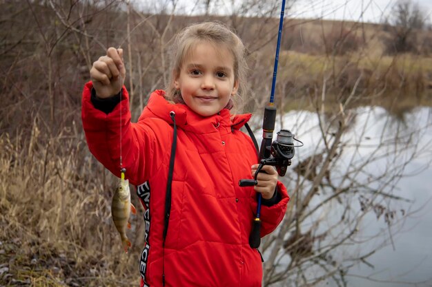 Petite fille dans une veste rouge avec un poisson dans ses mains