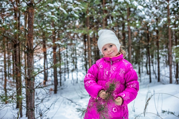 Petite fille dans des vêtements chauds jouant dans la forêt d'hiver, passant du temps à l'extérieur en hiver