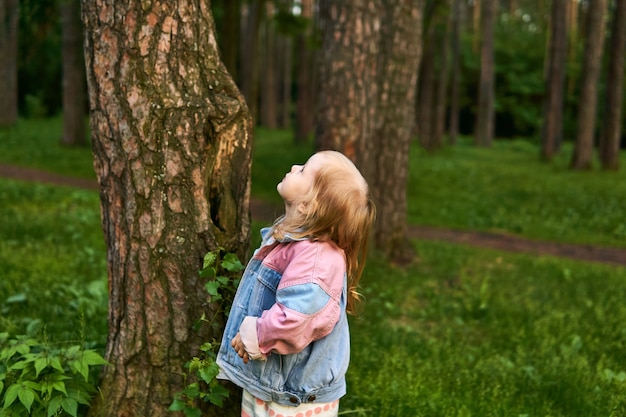 Petite fille debout à côté d'un arbre regarde sa couronne sur un fond naturel flou