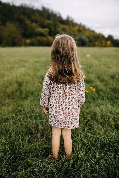 Une petite fille debout dans un champ avec de l'herbe verte portant une robe florale