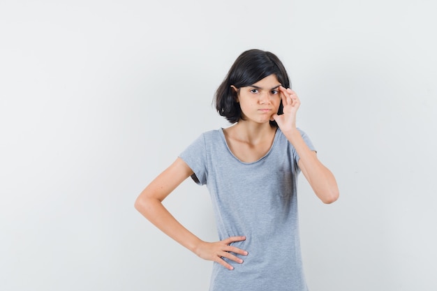 Petite fille debout dans la pensée pose en t-shirt et à la recherche hésitante. vue de face.