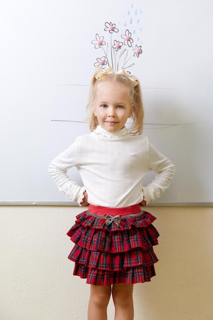 Petite fille debout près d'un tableau blanc dans une classe avec des fleurs dessinant sur un tableau