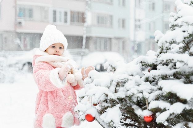 petite fille décore un arbre de Noël dans la cour.