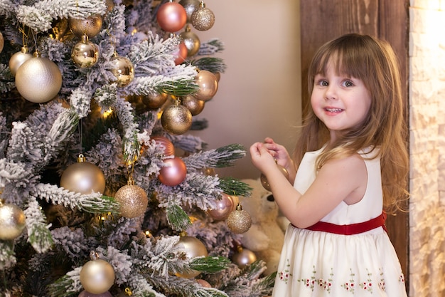 petite fille décore un arbre de Noël dans le salon avec des jouets