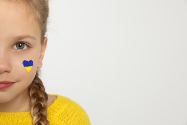 Petite fille avec le dessin du drapeau ukrainien sur le visage en forme de coeur sur fond blanc libre de l'espace pour le texte