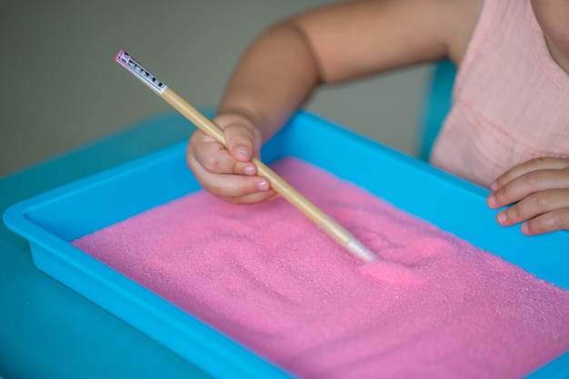 Petite fille dessinant sur le sable rose d'intérieur