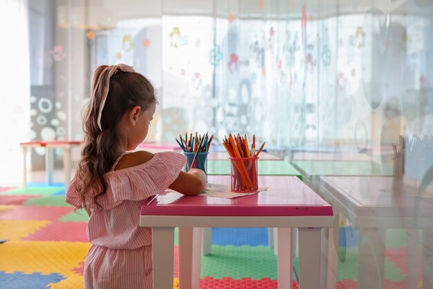 Petite fille dessinant avec un stylo de couleur en papier sur une table dans la salle de jeux, concept sain et préscolaire pour bébé