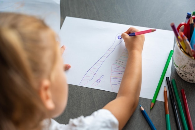 Une petite fille dessine avec des crayons de couleur à la maison.