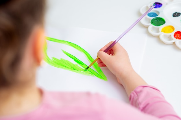 Petite fille dessine une feuille verte avec un pinceau à l'aquarelle sur un papier. Concept de jour de la terre.