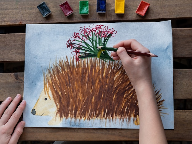 Photo petite fille dessine un hérisson avec des aquarelles et des crayons