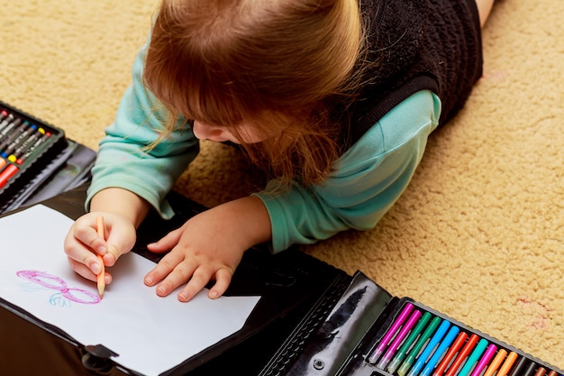 Petite fille dessine en se trouvant par terre.