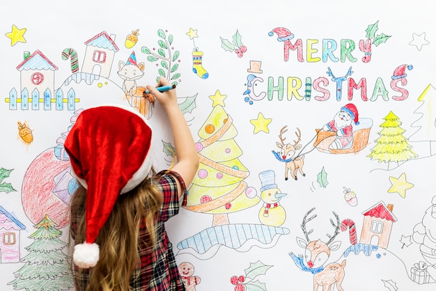 Petite fille dessiner des images de Noël sur un mur blanc