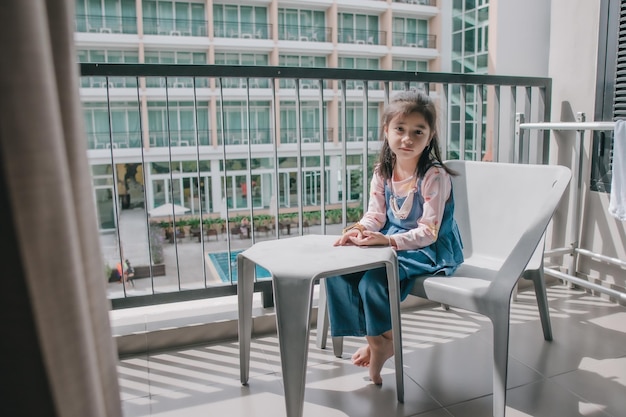 Photo une petite fille détendue assise dans une chaise sur le balcon.