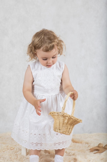 Une petite fille de deux ans vêtue d'une robe blanche joue avec ses jouets.