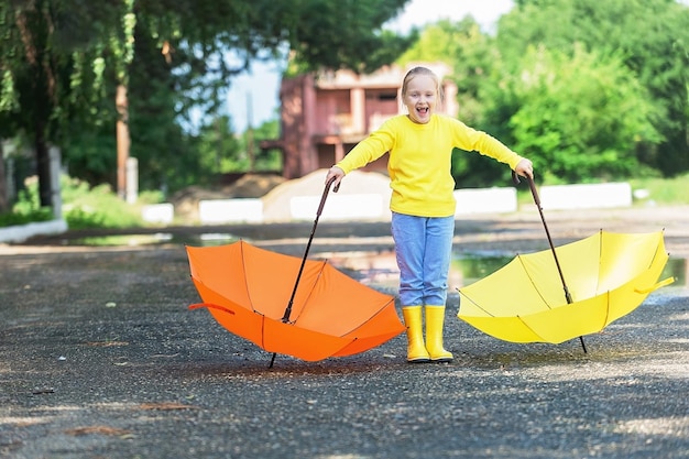 petite fille avec deux parapluies de couleur vive et des bottes en caoutchouc lors d'une promenade