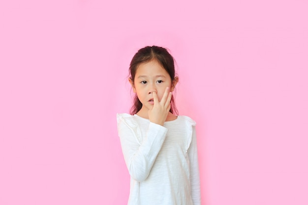 Petite fille avec le doigt dans son nez isolé sur fond rose