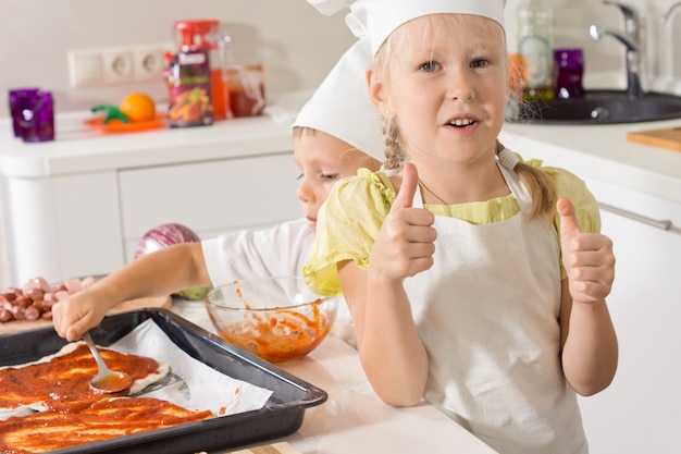 Petite fille donnant un coup de pouce alors qu'elle fait une pizza