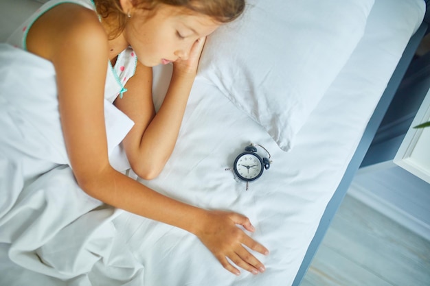 Petite fille dormant sur un grand et confortable linge de lit blanc l'après-midi à la maison