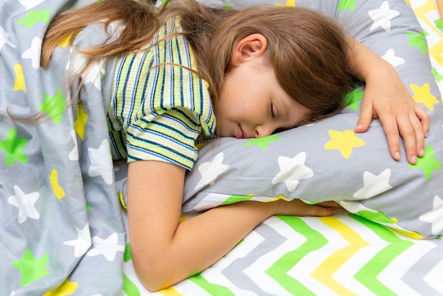 Une petite fille dort profondément dans son lit. Un sommeil approprié et sain pour les enfants.