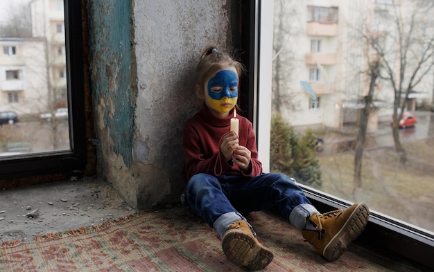 Une petite fille avec un drapeau ukrainien peint sur son visage priant tenant une bougie à la main pour la ville ukrainienne de Bucha est un geste de foi et d'espoir Les enfants contre la guerre